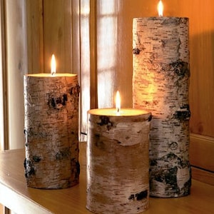 May include: Three birch bark candles with a natural wood grain pattern. The candles are lit and glowing.