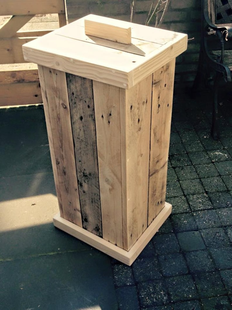 May include: A wooden trash can made from reclaimed pallet wood. The can has a hinged lid and a base made from the same wood.