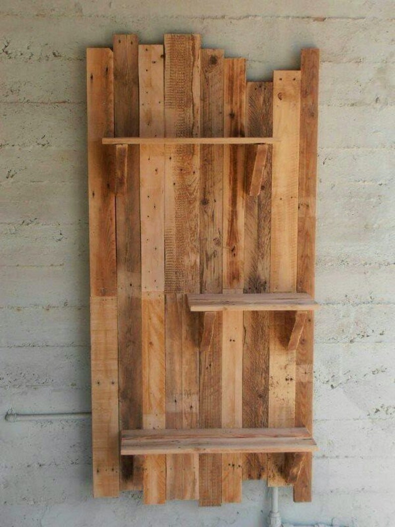 May include: A rustic wooden shelf unit made from reclaimed pallet wood. The shelf has three shelves and is mounted on a wall.