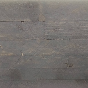 Op de afbeelding: Close-up van een grijs houten oppervlak met een natuurlijk houtnerfpatroon. Het hout is donkergrijs geverfd en heeft een rustieke uitstraling.