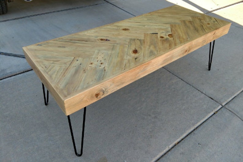 May include: A rectangular wooden coffee table with a light-colored, herringbone-patterned top. The table has a natural wood finish and is supported by four black hairpin legs. The table measures approximately 48 inches long.