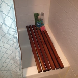 May include: A white bathtub with a wooden bath mat made of multiple slats. The mat is placed on the edge of the tub. There are two bottles of bath products and a pink bath sponge on the mat.