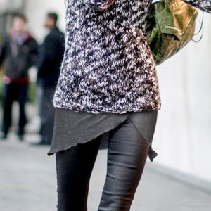 Puede incluir: Una mujer con un suéter estampado en blanco y negro, pantalones de cuero negro y botas negras. Lleva un bolso verde sobre el hombro.