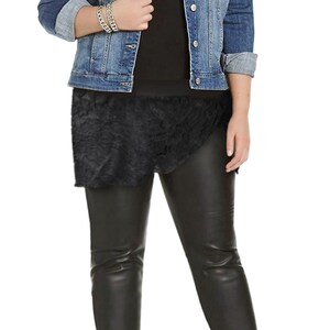 Op de afbeelding: Een vrouw draagt een blauw denim jack, een zwart shirt, een zwarte nep leren rok, zwarte nep leren leggings en zwarte hakken.