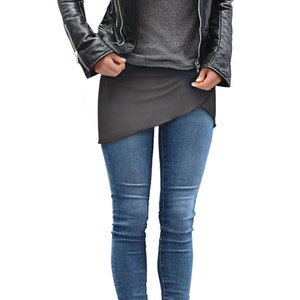 Op de afbeelding: Een vrouw draagt een zwart leren jack, een grijs shirt, een grijze wikkelrok, blauwe jeans en zwarte enkellaarsjes.