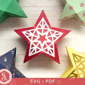 May include: A collection of colorful, geometric paper stars in red, green, yellow, and blue. The red star is the focal point, featuring a white, intricate star design. The image includes the text "SVG • PDF".