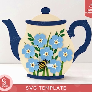 Peut inclure: Une découpe en papier en forme de théière avec un corps crème, une anse, un bec verseur et un couvercle bleu foncé. La théière est ornée de fleurs bleu clair, de tiges vertes et d'un petit motif d'abeille jaune et noire sur le devant.