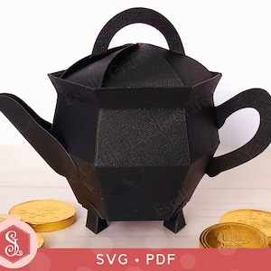May include: A black paper teapot with a handle, spout, and feet. The teapot is surrounded by gold-colored chocolate coins. The image includes the text "SVG • PDF" and the Essell Crafts logo.