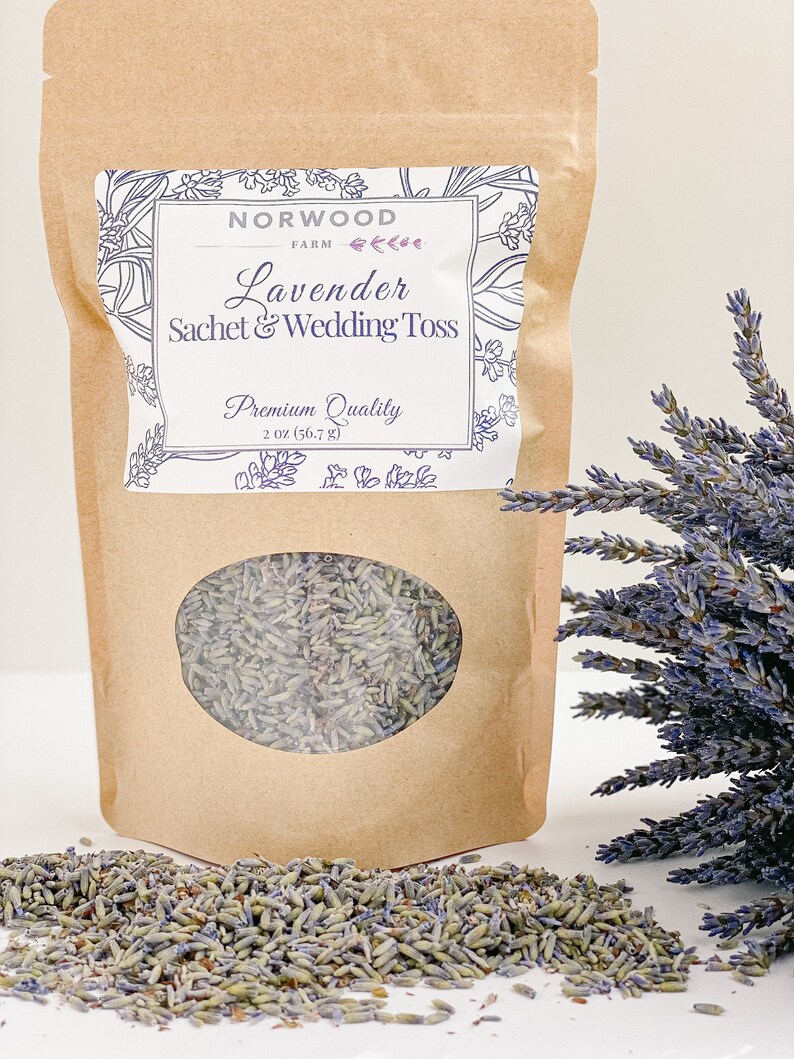 Puede incluir: Una bolsa de papel marr&oacute;n con una ventana transparente, llena de capullos de lavanda secos. La bolsa tiene una etiqueta que dice "Lavender Sachet & Wedding Toss" y "Premium Quality". Un manojo de lavanda seca y capullos sueltos est&aacute;n junto a la bolsa. La bolsa contiene 56,7 g de lavanda.