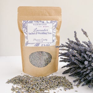 Puede incluir: Una bolsa de papel marr&oacute;n con saquitos de lavanda y para lanzar en bodas, con una ventana transparente. La etiqueta dice "Norwood Farm Lavender Sachet & Wedding Toss Premium Quality 56,7 g". Un ramo de lavanda est&aacute; a la derecha.