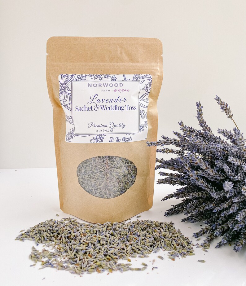 Puede incluir: Una bolsa de papel marr&oacute;n con saquitos de lavanda y para lanzar en bodas, con una ventana transparente. La etiqueta dice "Norwood Farm Lavender Sachet & Wedding Toss Premium Quality 56,7 g". Un ramo de lavanda est&aacute; a la derecha.