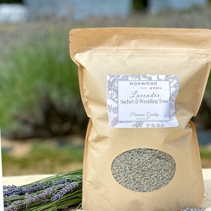 Puede incluir: Una bolsa de papel marr&oacute;n de saquito de lavanda y lanzamiento de boda con una ventana transparente, etiquetada como "Norwood Farm". Un manojo de lavanda y capullos de lavanda sueltos est&aacute;n junto a la bolsa. La bolsa contiene 227 g de lavanda de primera calidad.