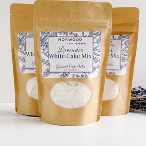 May include: Three brown paper bags with white cake mix inside. The center bag has a label that reads "NORWOOD FARM Lavender White Cake Mix Gourmet Cake Mix 10.5 oz (297 g)".