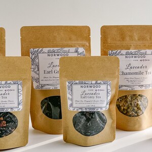 May include: Six brown paper bags with clear windows, each containing a different type of loose leaf tea. The bags are labeled with the text "Norwood Farm" and the type of tea, including "Lavender Rose Tea", "Lavender Earl Grey Tea", and "Lavender Chamomile Tea".