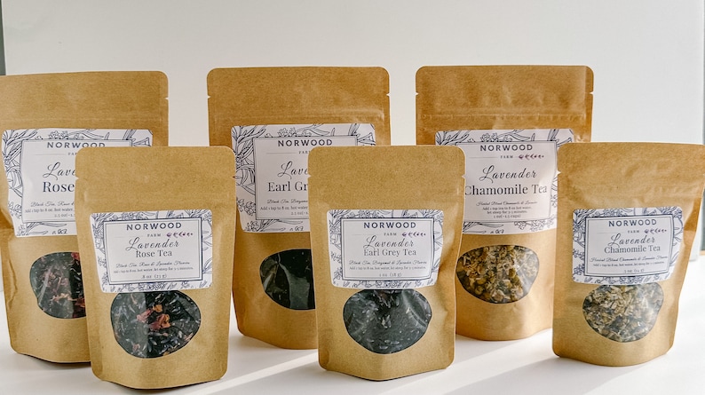 May include: Six brown paper bags with clear windows, each containing a different type of loose leaf tea. The bags are labeled with the text "Norwood Farm" and the type of tea, including "Lavender Rose Tea", "Lavender Earl Grey Tea", and "Lavender Chamomile Tea".