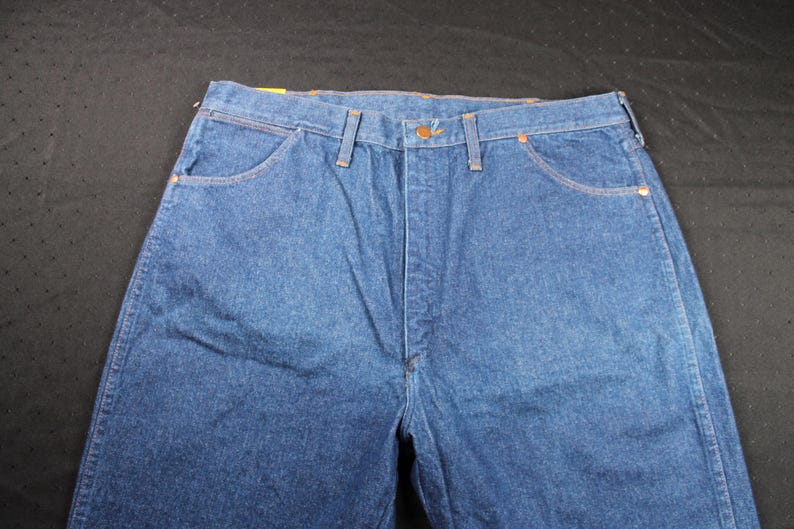 May include: A pair of blue denim jeans with a button fly and belt loops. The jeans have two front pockets and two back pockets.