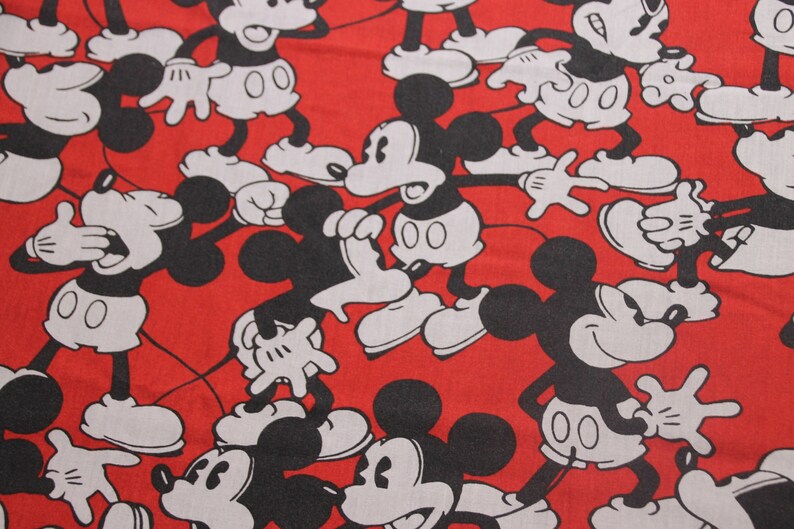 Op de afbeelding: Rode stof met een herhalend patroon van zwarte en witte Mickey Mouse-figuren. De figuren staan in verschillende poses, waaronder zwaaien, glimlachen en er verrast uitzien.