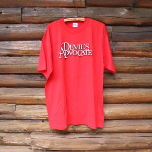 May include: Red t-shirt with the words "Devil's Advocate" printed in white on the front.