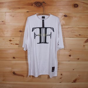 May include: White oversized t-shirt with a black and gold "FUBU" logo on the front.