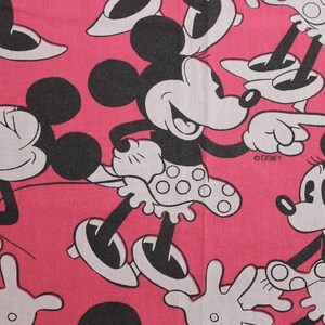 Peut inclure: Tissu rose avec un motif r&eacute;p&eacute;t&eacute; de Minnie Mouse dans diverses poses. Minnie est repr&eacute;sent&eacute;e en noir et blanc avec sa jupe &agrave; pois signature. Le logo Disney est visible dans le motif.