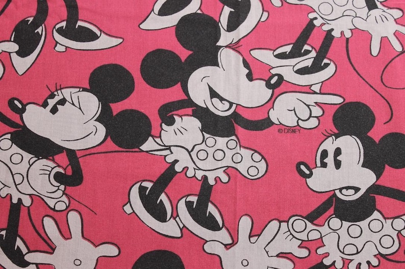 Peut inclure: Tissu rose avec un motif r&eacute;p&eacute;t&eacute; de Minnie Mouse dans diverses poses. Minnie est repr&eacute;sent&eacute;e en noir et blanc avec sa jupe &agrave; pois signature. Le logo Disney est visible dans le motif.