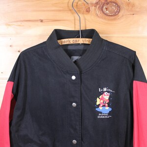 K&ouml;nnte beinhalten: Schwarze und rote Baseballjacke mit einem Cartoon-Fisch-Motiv und dem Text "I'm Waterin' for Junior Duracell".