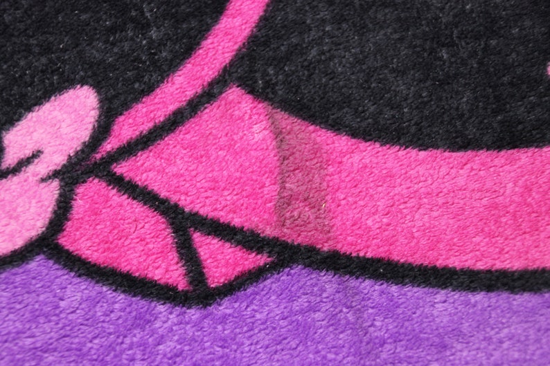 Pode incluir: Close-up de um tecido estampado em rosa e preto com textura felpuda. O tecido tem um contorno preto e um fundo rosa.