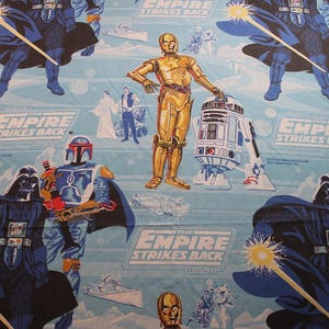 May include: Light blue Star Wars themed fabric featuring Darth Vader, C-3PO, R2-D2, and Boba Fett. The text "THE EMPIRE STRIKES BACK" is repeated throughout the design. The fabric has a repeating pattern of characters and scenes.