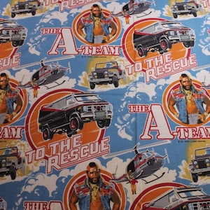 May include: Fabric with a repeating pattern featuring images of the A-Team. The design includes the A-Team logo, the phrase "To the Rescue," and illustrations of the cast, vehicles, and helicopters. The background is light blue.