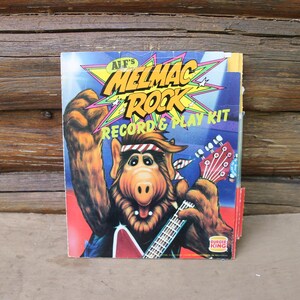 May include: A vintage ALF's Melmac Rock Record & Play Kit box. The box features a cartoon illustration of ALF playing a guitar. The background is a wooden surface. The Burger King logo is visible.