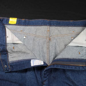 May include: A pair of blue denim jeans with a zipper fly and button closure. The jeans have a light blue lining and a yellow tag on the waistband.