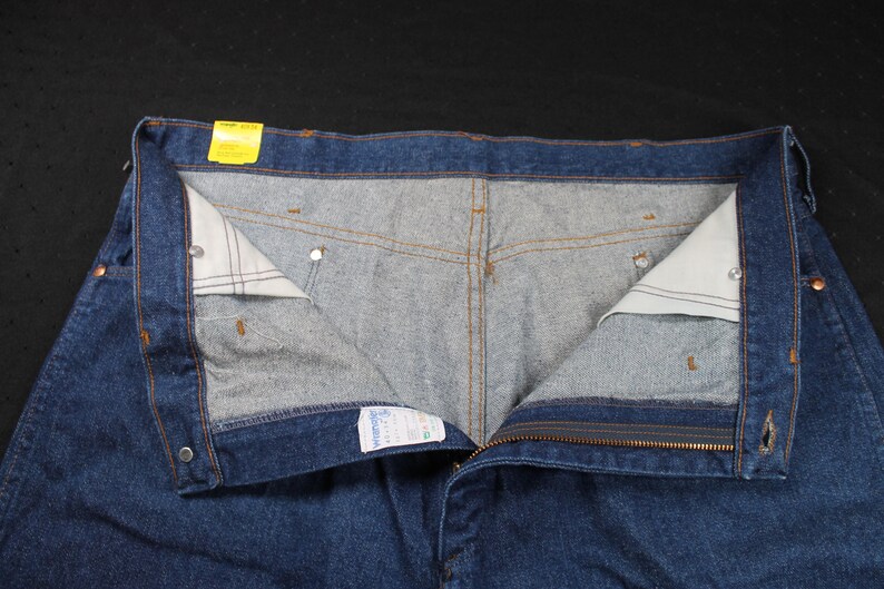 May include: A pair of blue denim jeans with a zipper fly and button closure. The jeans have a light blue lining and a yellow tag on the waistband.