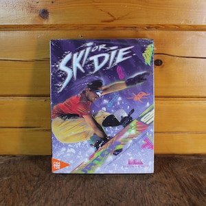 May include: A vintage video game box for "Ski or Die" featuring a skier on a snowboard. The box has a purple background with neon graphics and the game's title in white. The C64 and 128 logos are visible.