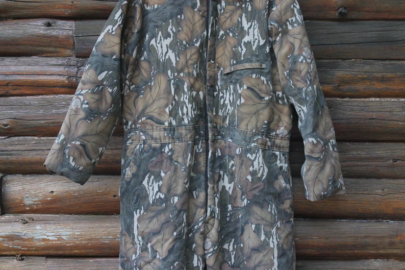 Puede incluir: Mono de camuflaje con cremallera completa, bolsillo y mangas largas. El mono presenta un dise&ntilde;o de hojas marrones, grises y blancas. La prenda est&aacute; hecha de un material duradero, adecuado para actividades al aire libre.