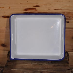 May include: A white enamel baking dish with a blue rim. The dish is square and has a smooth, glossy finish.