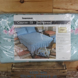 Może przedstawiać: Jasno błękitna narzuta na łóżko z kwiatowym wzorem i falbanką. Narzuta jest zapakowana w plastik i oznaczona etykietą "Lawrence Couvre-lit - Bedspread Double".