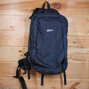 Peut inclure: Un sac à dos noir avec une poche zippée à l'avant et des bretelles réglables. Le sac à dos porte le logo "Mountain Equipment Co-op" imprimé sur le devant.