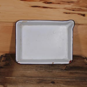 May include: White enamel baking dish with a black rim and a red interior. The dish is sitting on a wooden surface.