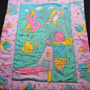 Könnte beinhalten: Eine violette und grüne Babydecke mit Patchwork-Muster, das verschiedene Tiere und Buchstaben zeigt. Die Decke hat einen rosa Rand mit kleinen rosa Herzen.