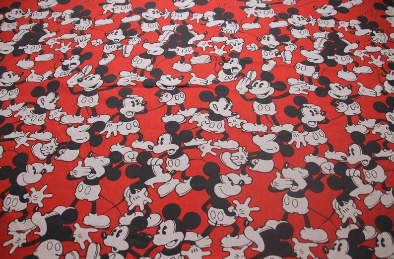 Op de afbeelding: Rode stof met een herhalend patroon van zwarte en witte Mickey Mouse-silhouetten. De Mickey Mouse-figuren staan in verschillende poses, sommige met hun handen omhoog, sommige met hun handen omlaag en sommige met hun mond open.