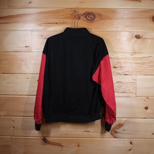 K&ouml;nnte beinhalten: Eine schwarze und rote Jacke mit Rei&szlig;verschluss. Die Jacke hat lange &Auml;rmel und einen Stehkragen.