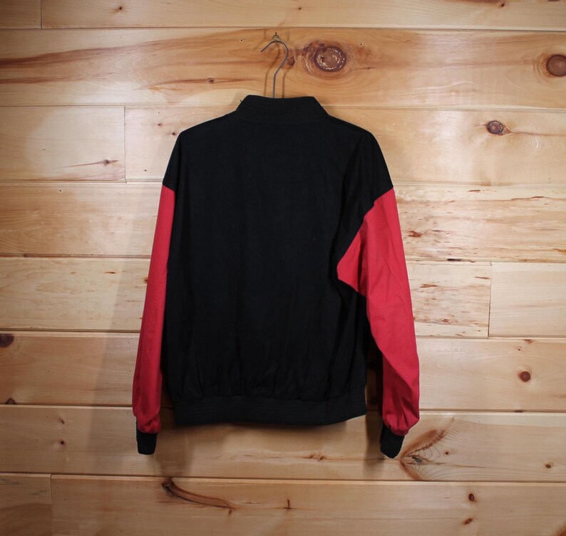 K&ouml;nnte beinhalten: Eine schwarze und rote Jacke mit Rei&szlig;verschluss. Die Jacke hat lange &Auml;rmel und einen Stehkragen.