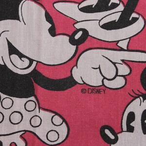 Peut inclure: Gros plan sur un tissu rose avec un motif r&eacute;p&eacute;t&eacute; de Mickey et Minnie Mouse. Les personnages sont en noir et blanc, Minnie portant une jupe &agrave; pois. Le logo Disney est visible.