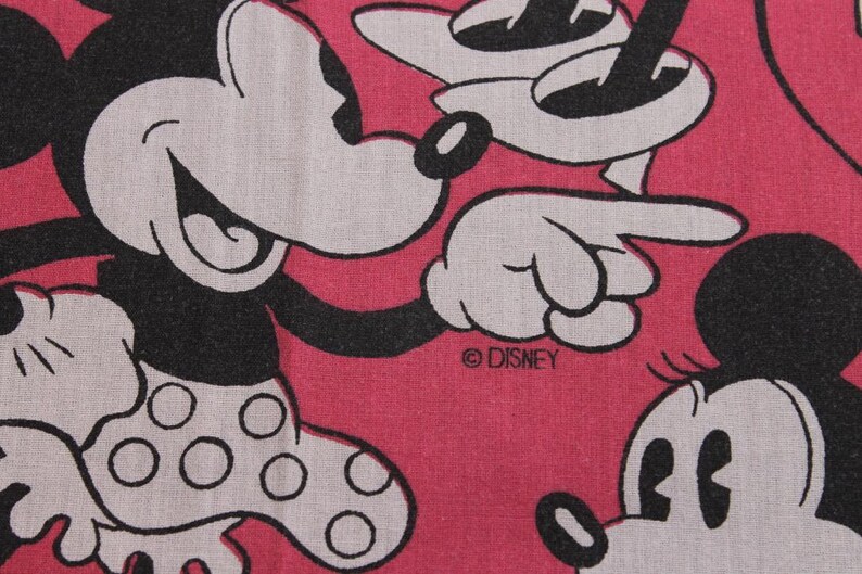 Peut inclure: Gros plan sur un tissu rose avec un motif r&eacute;p&eacute;t&eacute; de Mickey et Minnie Mouse. Les personnages sont en noir et blanc, Minnie portant une jupe &agrave; pois. Le logo Disney est visible.