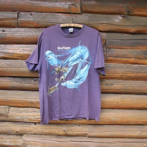May include: Purple Six Flags World of Adventure t-shirt featuring a graphic of dolphins and sea turtles.