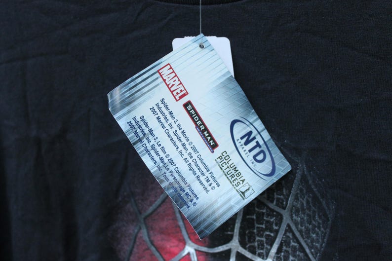 May include: A black t-shirt featuring a rectangular hang tag with the Marvel logo, Spider-Man 3 branding, and Columbia Pictures text. The tag includes copyright information for 2007 Marvel Characters, Inc. and Columbia Pictures Industries, Inc.