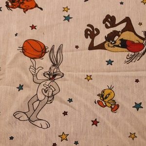 Könnte beinhalten: Ein weißer Stoff mit einem Cartoon-Druck von Bugs Bunny, Tweety Bird, Taz und Sylvester. Der Hintergrund ist mit Sternen gefüllt.