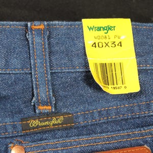 May include: Blue denim jeans with a brown leather patch and a yellow Wrangler tag that says "40081 PW 40X34" and has a barcode.