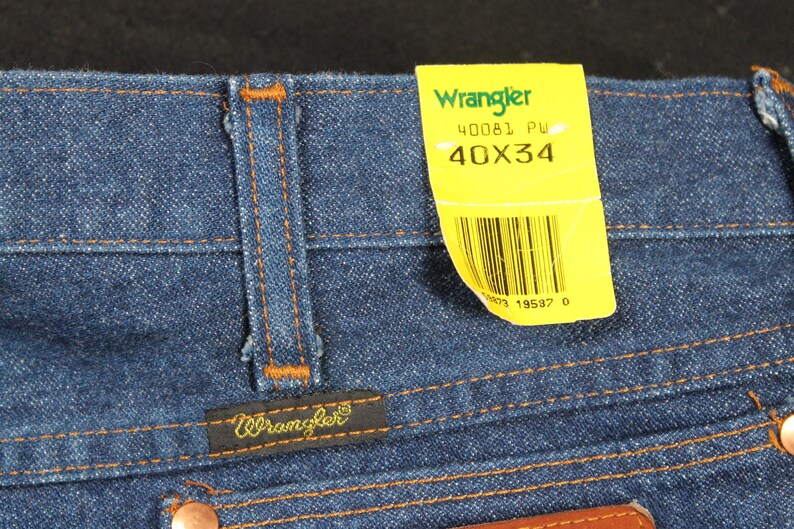 May include: Blue denim jeans with a brown leather patch and a yellow Wrangler tag that says "40081 PW 40X34" and has a barcode.