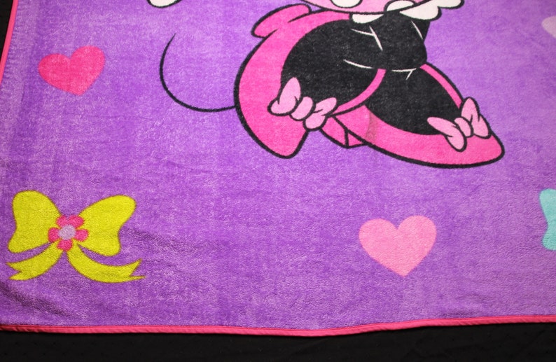Pode incluir: Cobertor de l&atilde; polar roxo com um personagem de desenho animado rosa vestindo um vestido preto e sapatos rosa. O personagem est&aacute; rodeado de cora&ccedil;&otilde;es rosas e um la&ccedil;o amarelo.